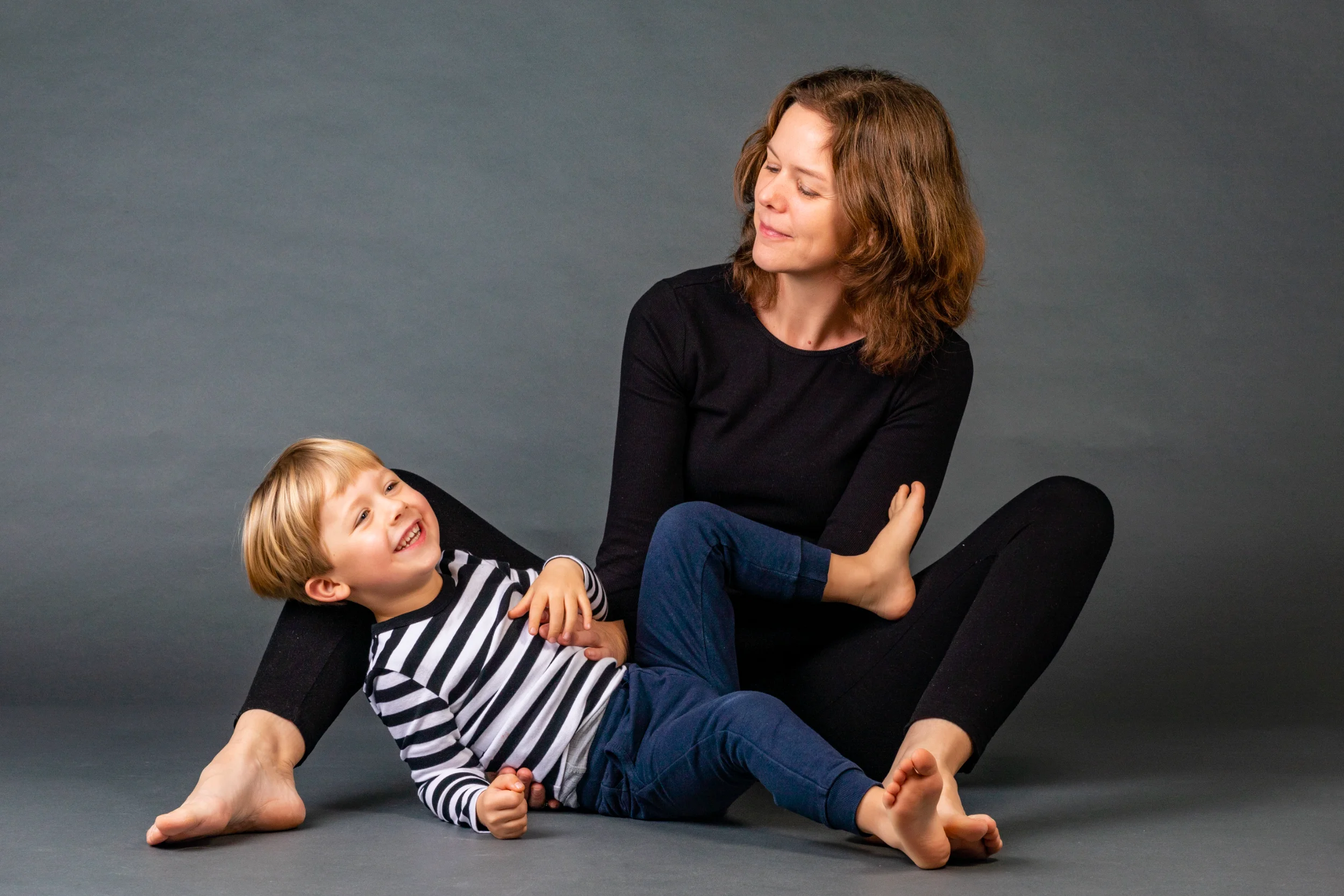 Glad mor og smilende søn i sort/hvid stribet trøje, der leger og hygger sig til familiefotografering.