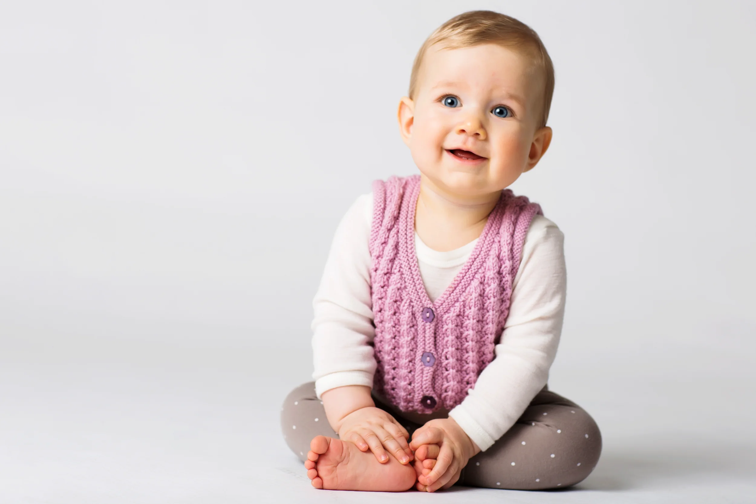 Glad baby med strålende blå øjne i pink vest til Virum babyfotografering, siddende med fokus og et smil.
