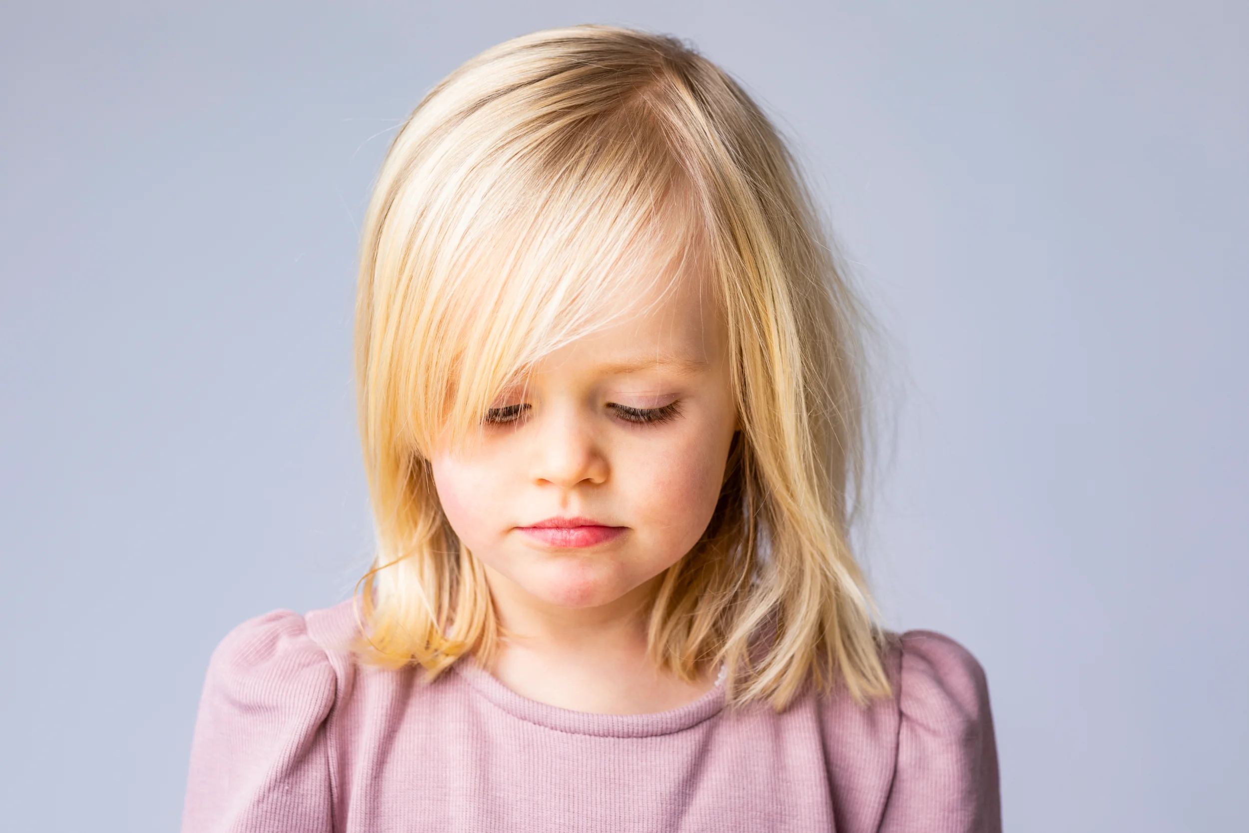 Nærbillede af et barn med blondt hår, der kigger ned. Billedet er et autentisk børneportræt med naturligt lys.