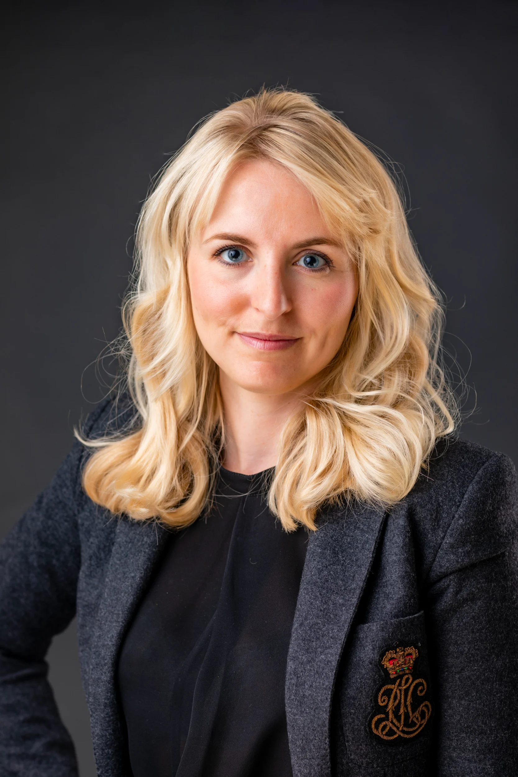 Nærbillede af kvinde med blondt hår og intense blå øjne, klædt i mørk blazer, et ægte portrætfoto.