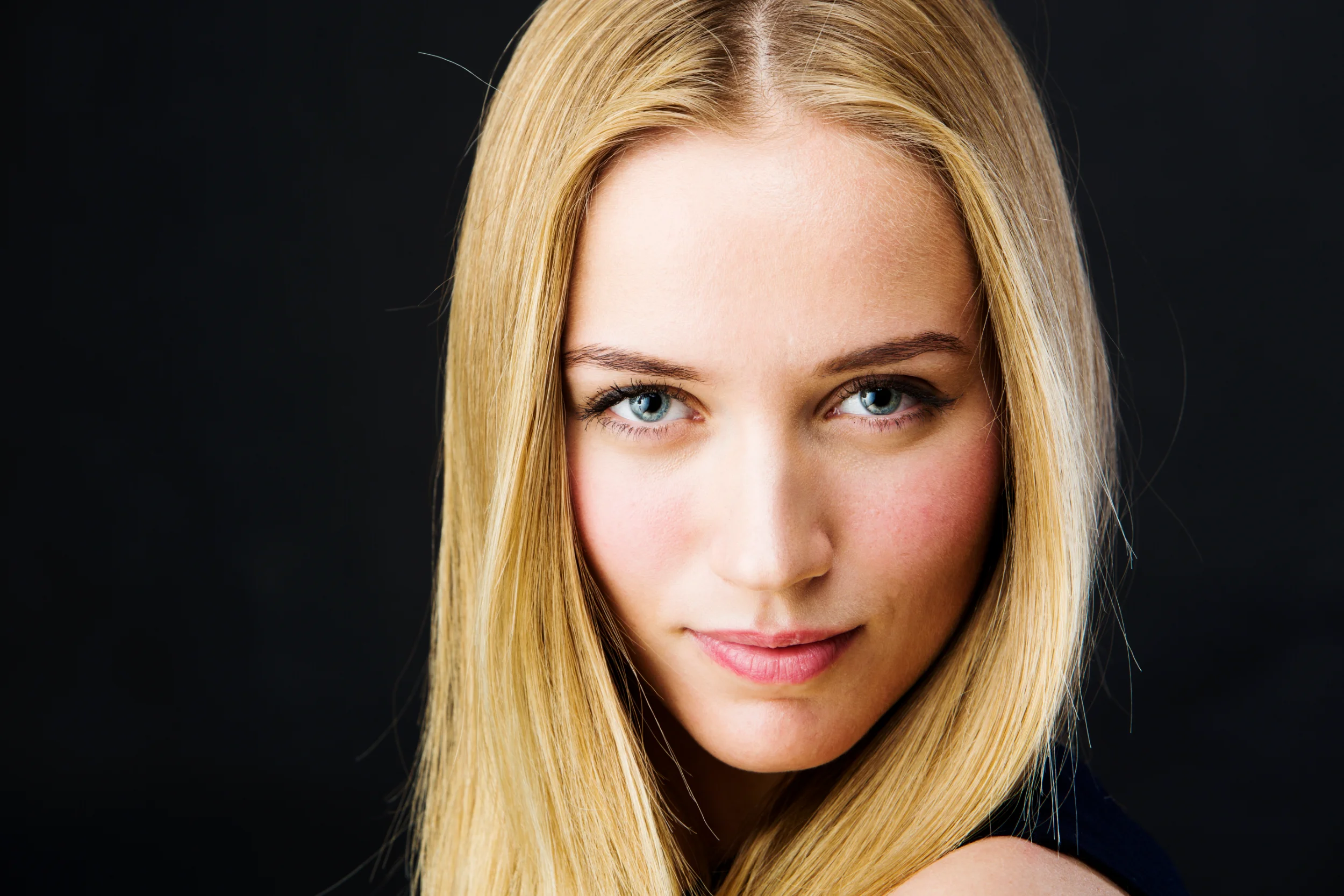 Nærbillede portrætfoto af blond kvinde med strålende blå øjne og blødt lys mod mørk baggrund.