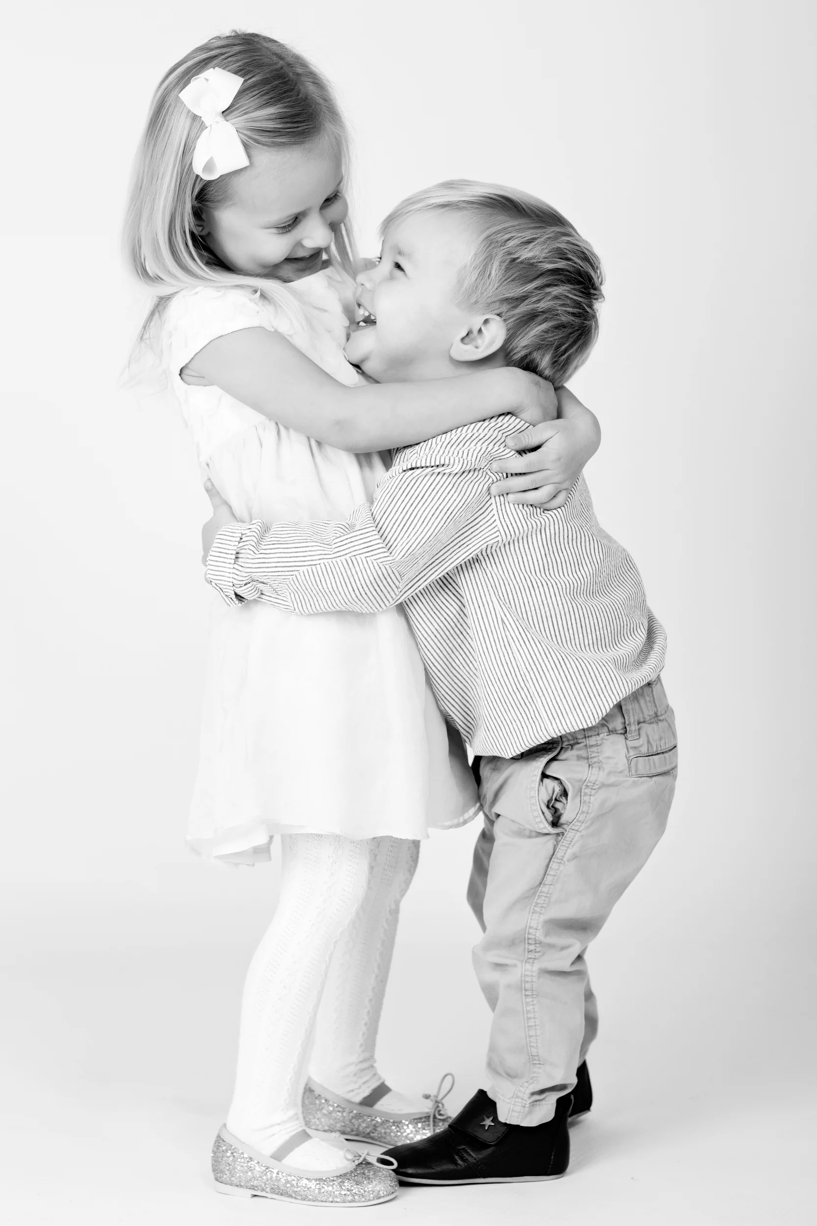 Sort/hvidt børnefotografi af glad pige og dreng, der omfavner hinanden i blødt lys.