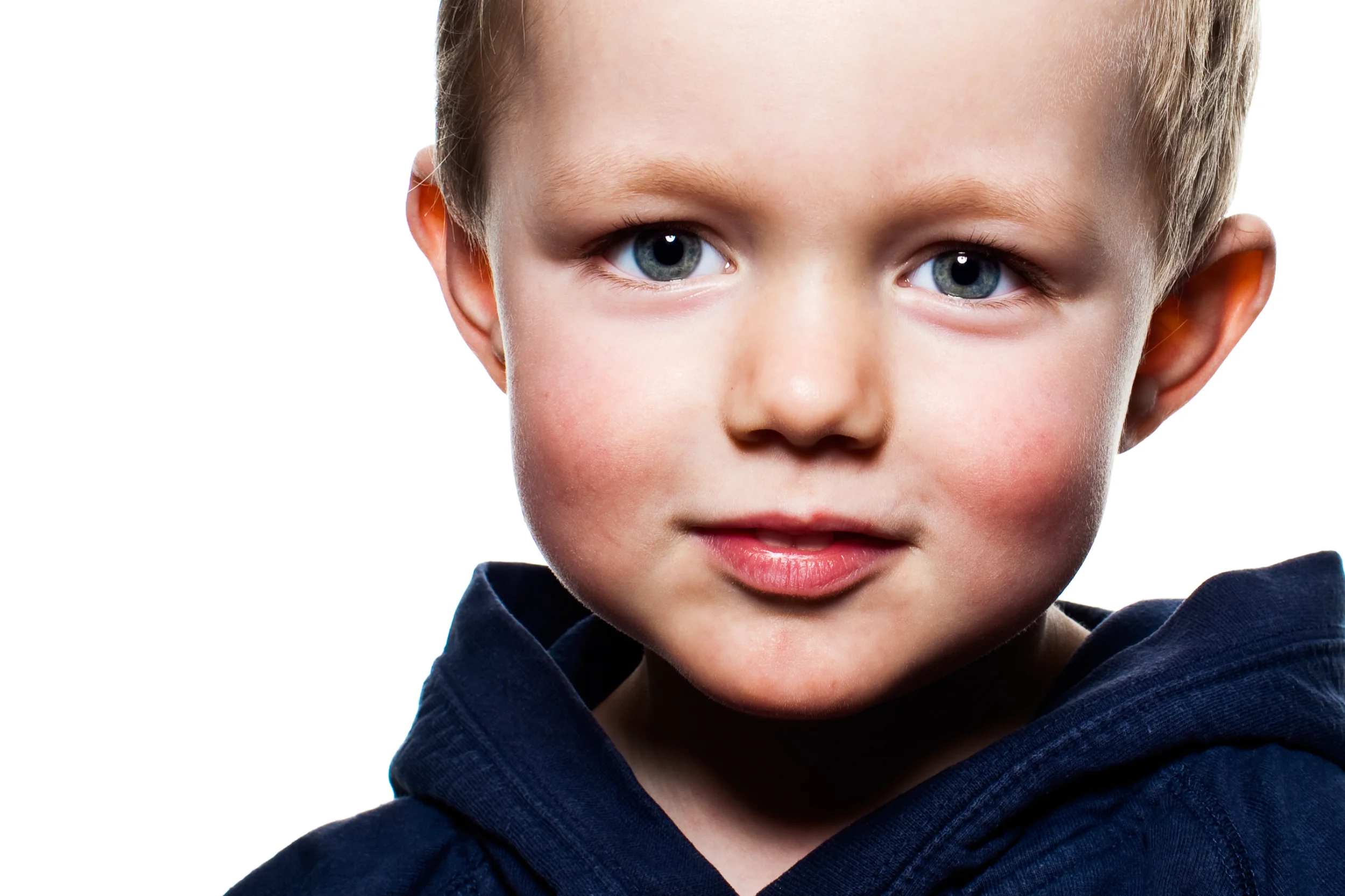 Børnefoto: Nærbillede af smilende dreng med glimt i øjet og rød kinder iført mørkeblå hættetrøje.