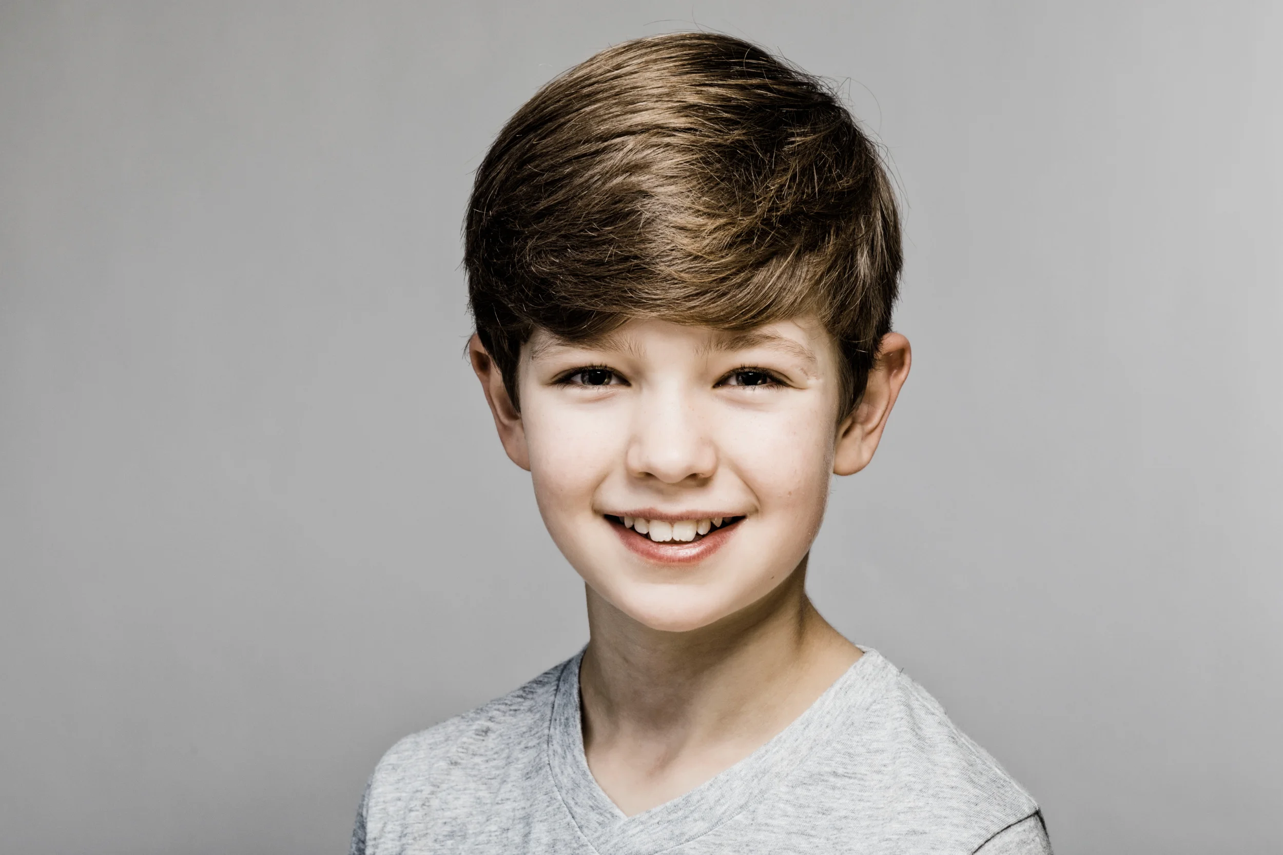 Nærbillede af glad dreng med smil og brunt hår, naturligt børneportræt med blød belysning i Virum. Fotografering af børn.
