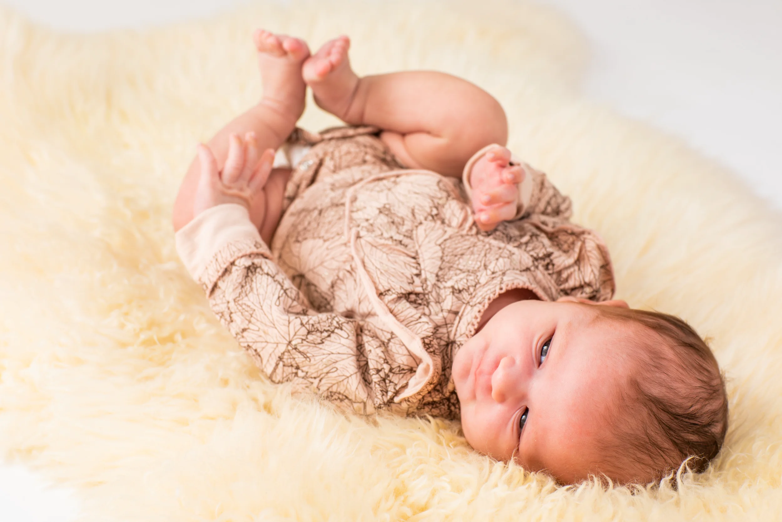 Autentisk babyfotografering – Nyfødt baby i mønstret tøj ligger legende på ryggen på hvidt, blødt tæppe.
