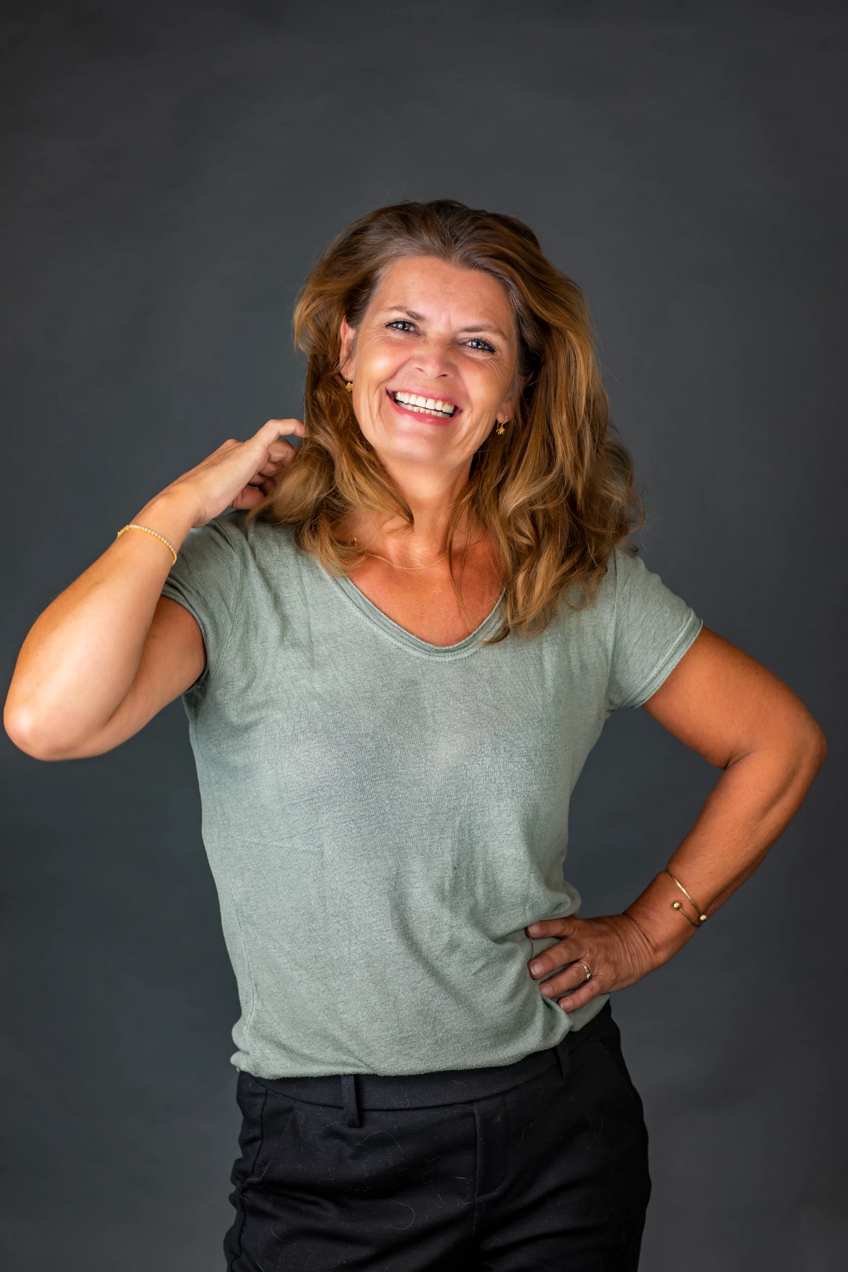 Glad kvinde med smil i ansigtet, grønt tøj og brunt hår foran grå baggrund, et charmerende portrætfoto.