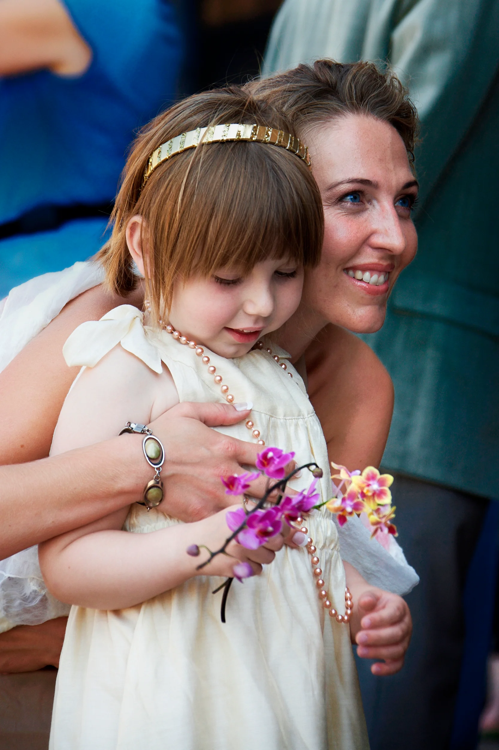 Bryllupsfotografi: Mor krammer sin datter, begge smiler, datteren holder en orkidé og bærer perlekæde og hårbånd.