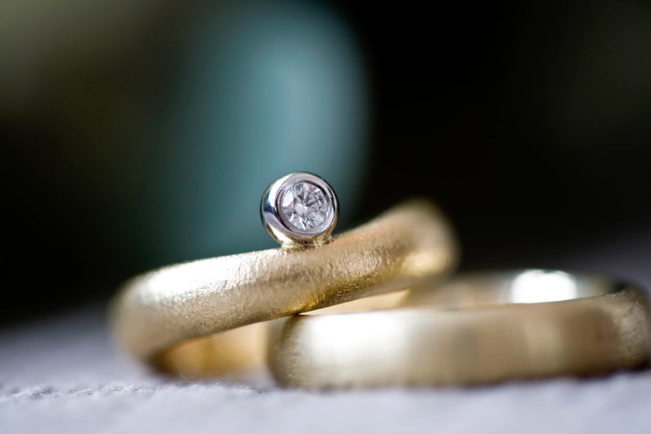 Nærbillede af et par matte guldbryllupsringe. Den ene har en skinnende diamant.