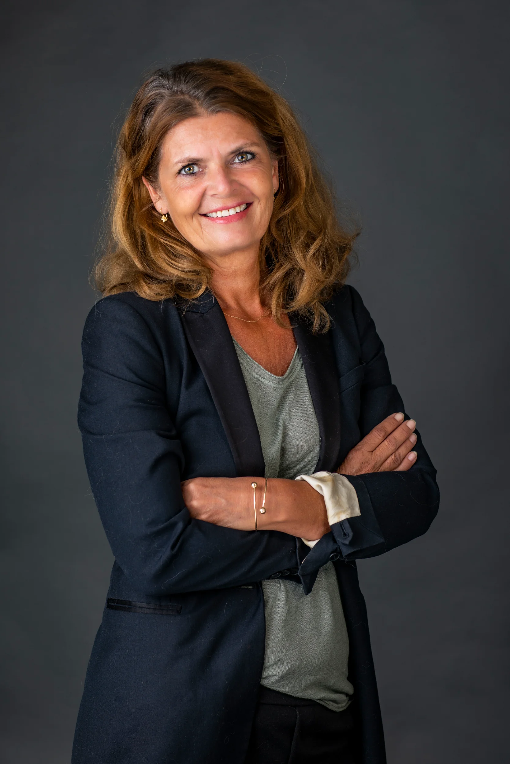 Portrætfoto af smilende kvinde med lysebrunt hår og sorte øjne, iført sort jakke og grå bluse.