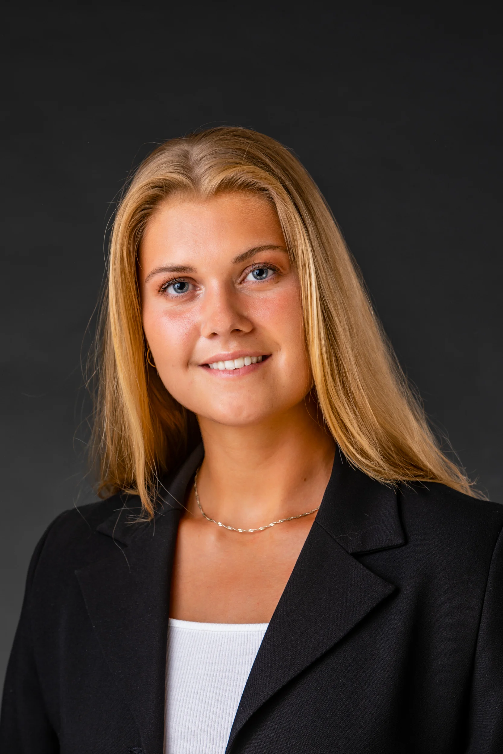 Portrætfoto af smilende ung kvinde med langt blondt hår og blå øjne i sort blazer fotograferet i studie.