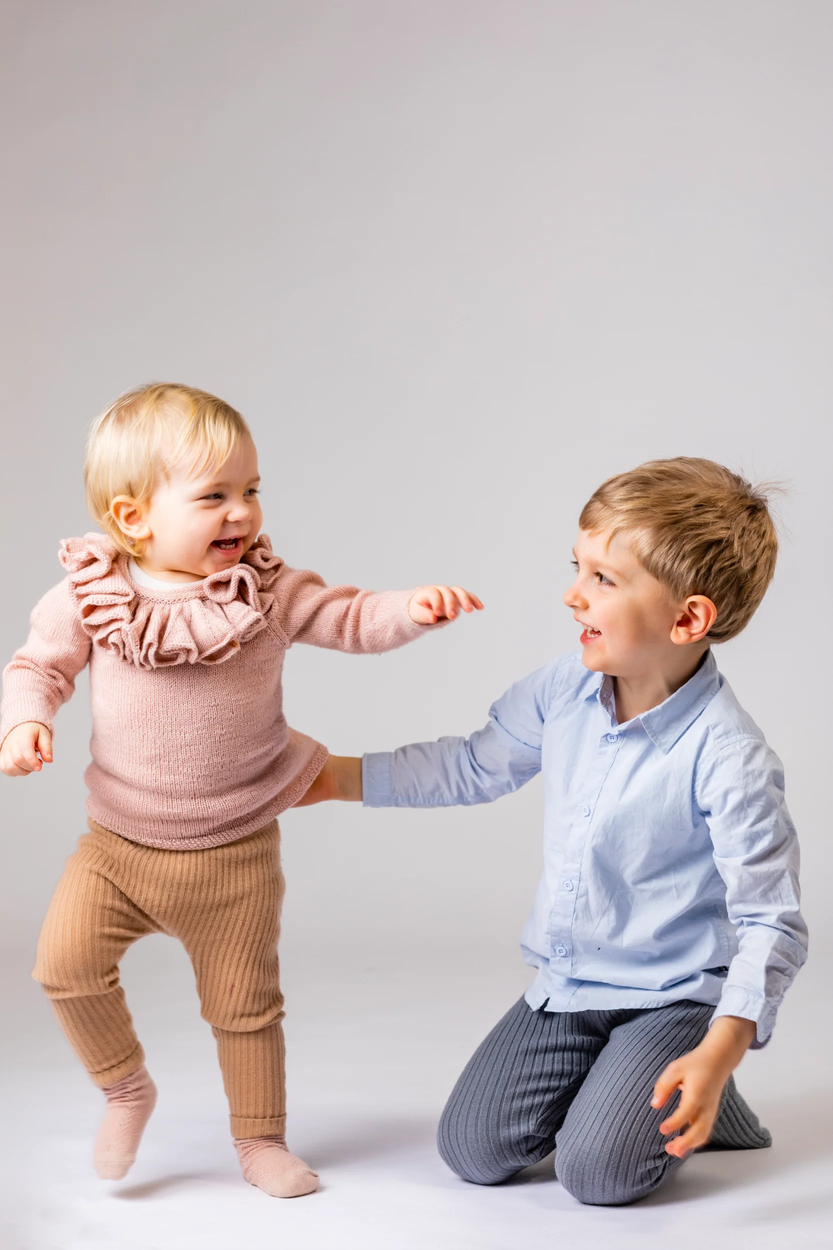 Børn: En glad lille pige i lyserød bluse tager de første skridt, mens hendes storebror i lyseblå skjorte støtter og smiler.