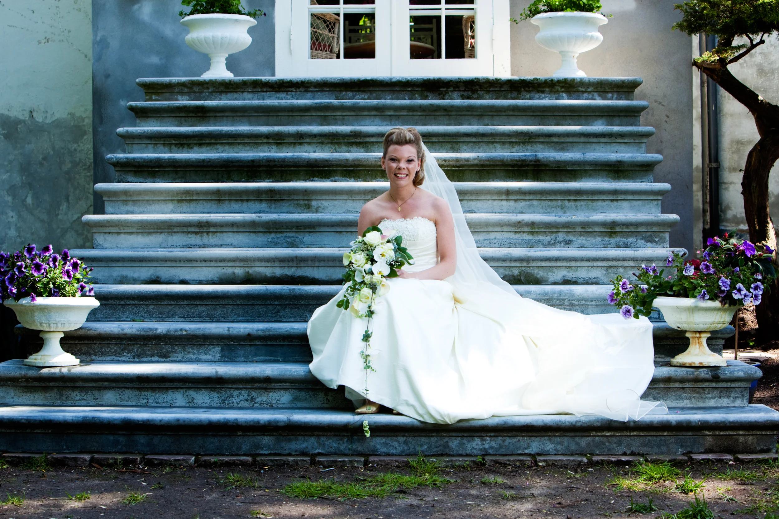 Brud i smuk kjole på trappe med blomster