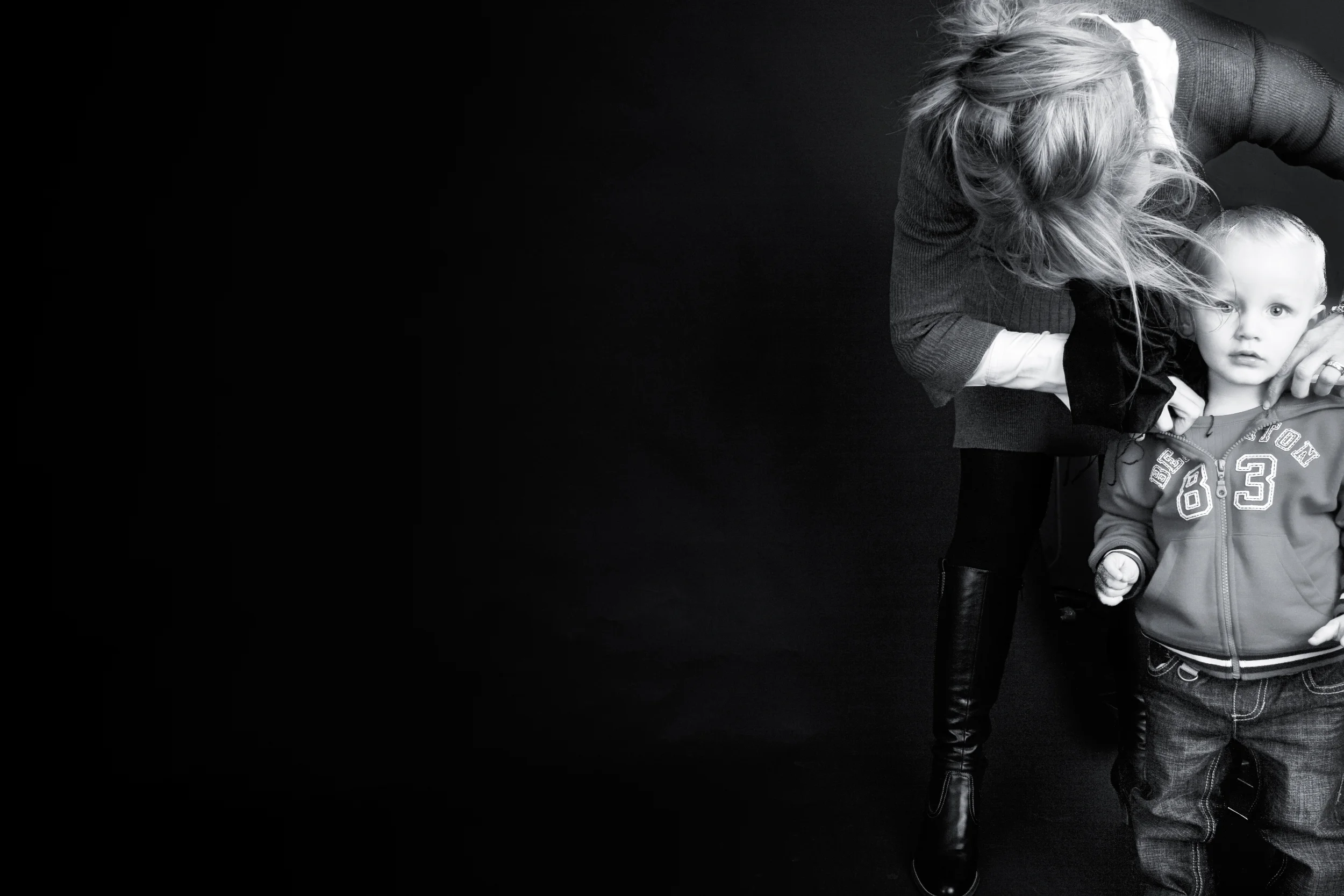 Børneportræt i sort/hvid af en mor med bøjet hoved, der ømt holder om sin søn mod en mørk baggrund.