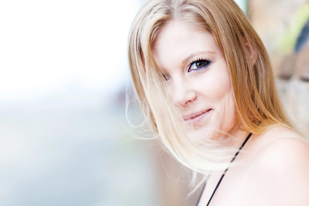 Nærbillede af ung kvinde med langt blondt hår og et charmerende smil, der kigger direkte ind i kameraet. Et personligt por...