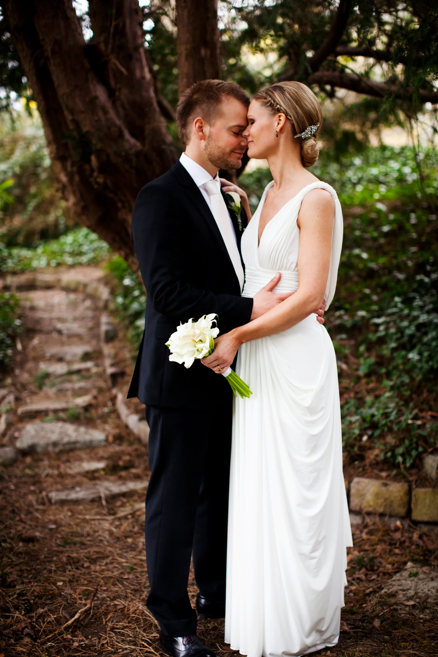 Bryllupsbillede af nygift par tæt omfavnet i sort/hvid, med blød stemning og naturligt lys i baggrunden.