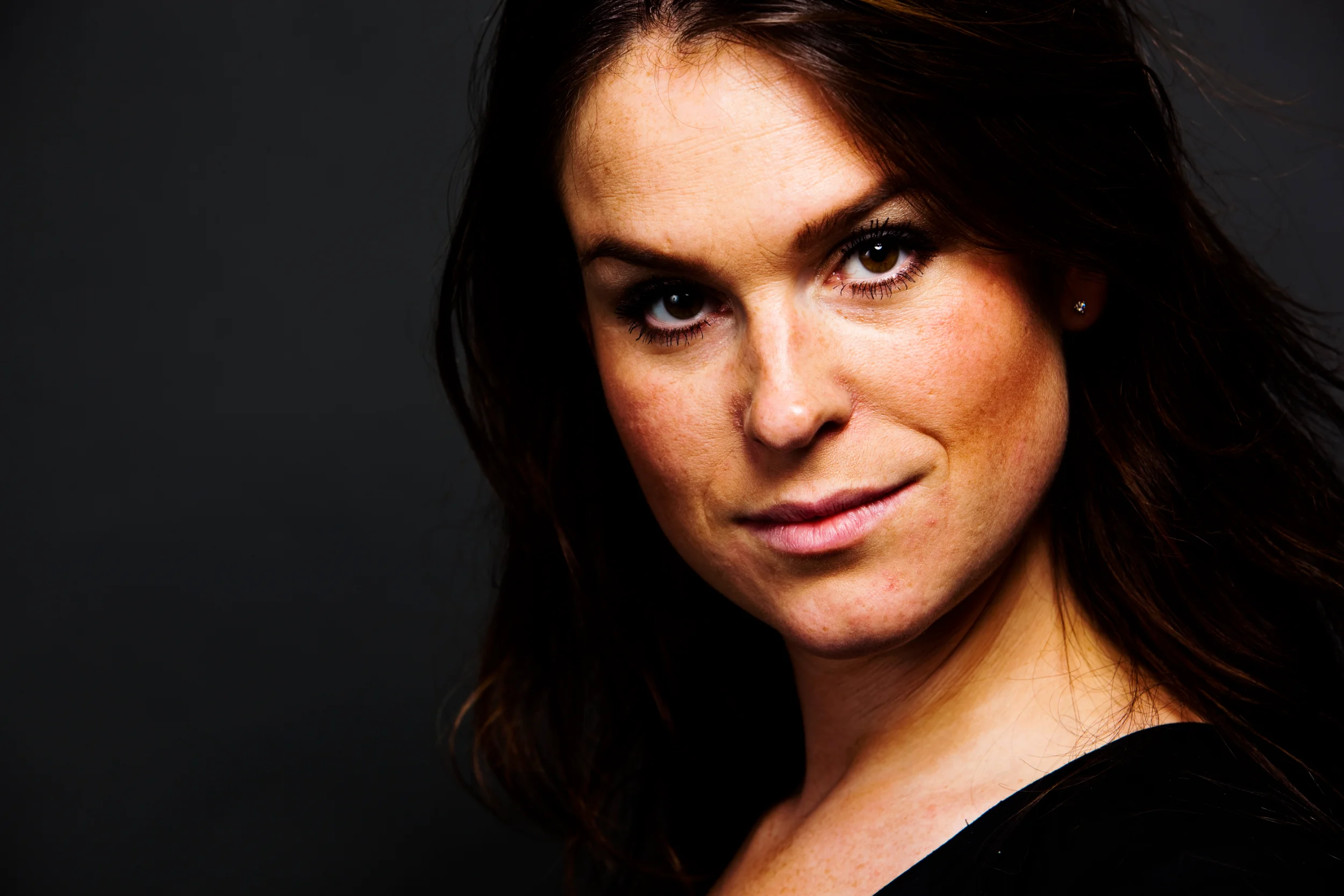 Professionelt portrætfoto af smilende kvinde med brunt hår mod mørk baggrund, flot belysning i Virum.
