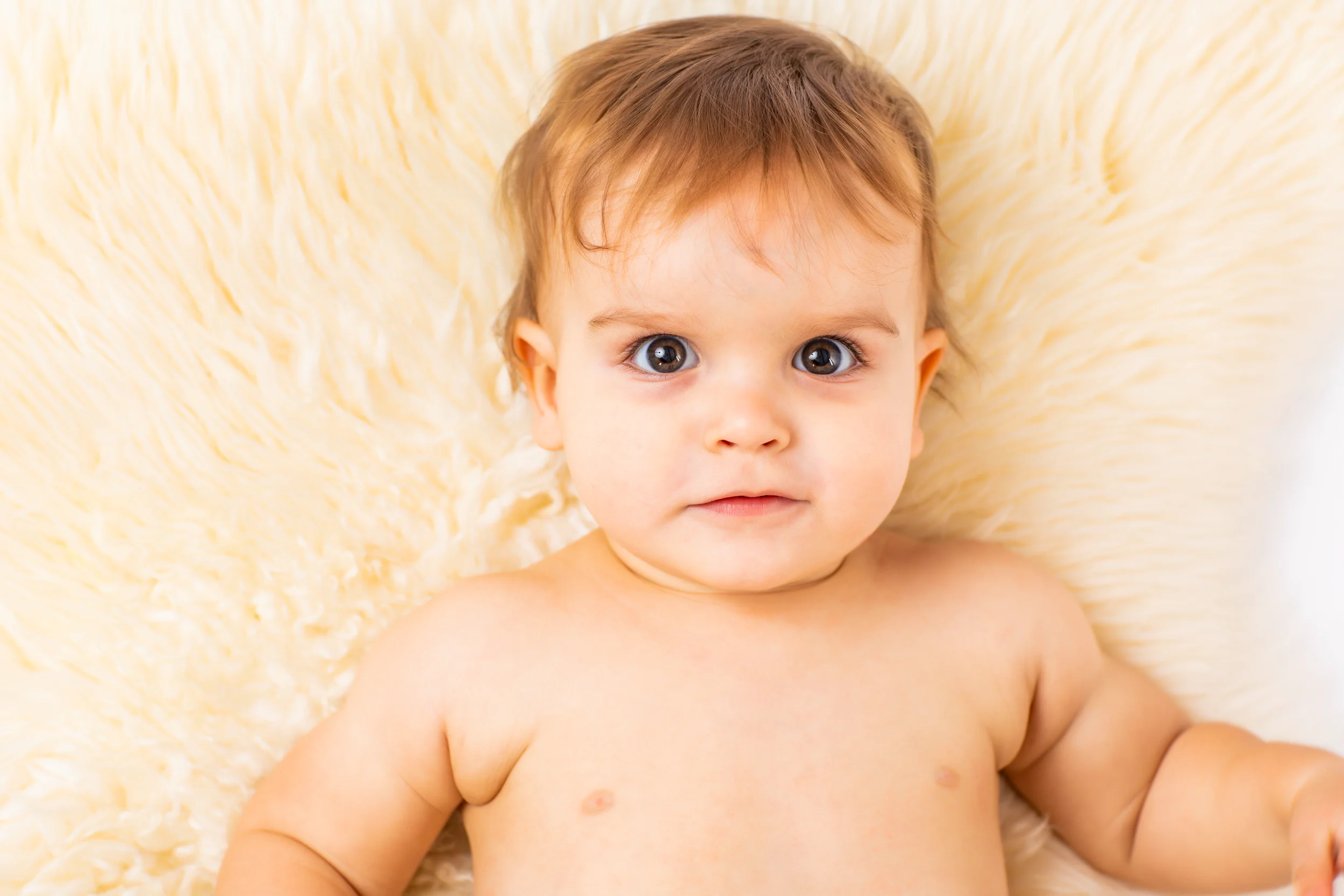 Nærbillede af baby liggende på blødt, hvidt fåreskind. Virums babyfotografering med store brune øjne og nysgerrigt udtryk.