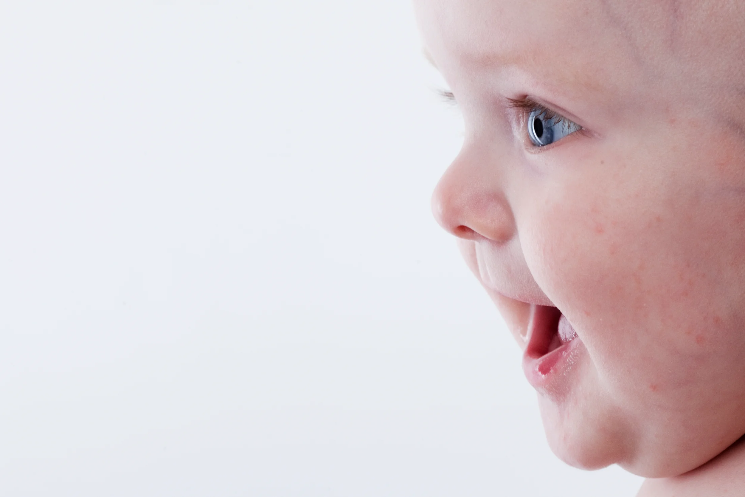 Nærbillede af nysgerrig baby i sort/hvid, der ser opmærksomt mod højre med åben mund. Et charmerende babyfotografi.