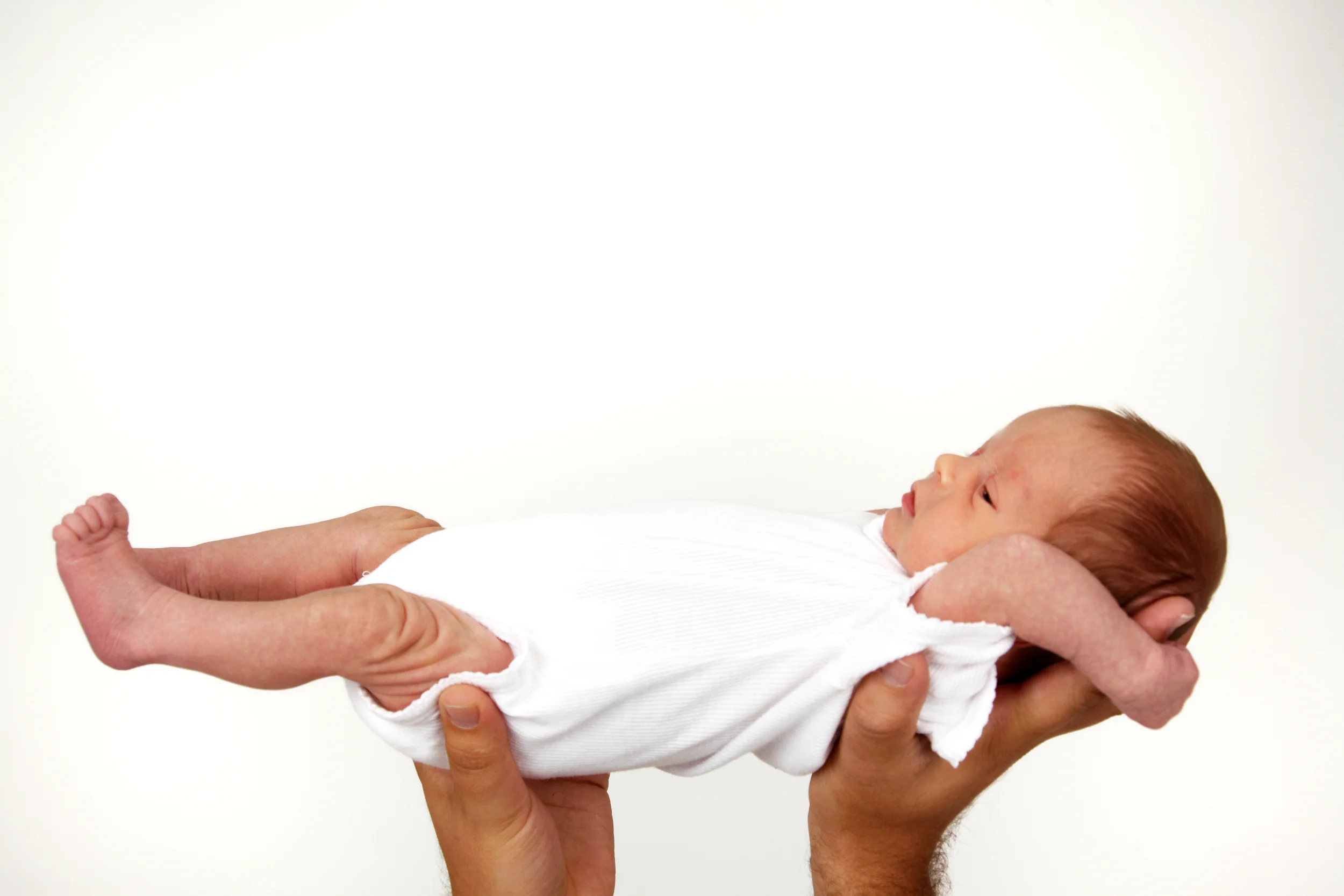 Nyfødt baby holdes forsigtigt i hænderne mod en lys baggrund, et sødt babybillede der udstråler tryghed og ro.