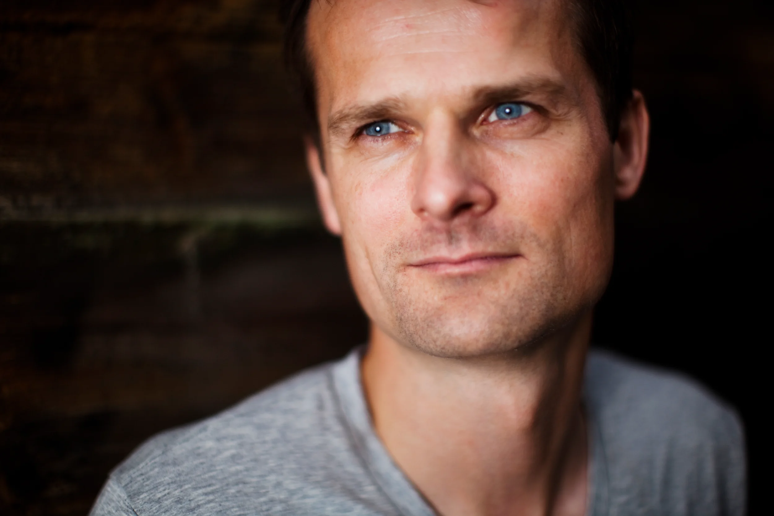 Nærbillede af mand med intense blå øjne kigger opmærksomt mod højre. Et følelsesladet portrætfoto med blødt lys.