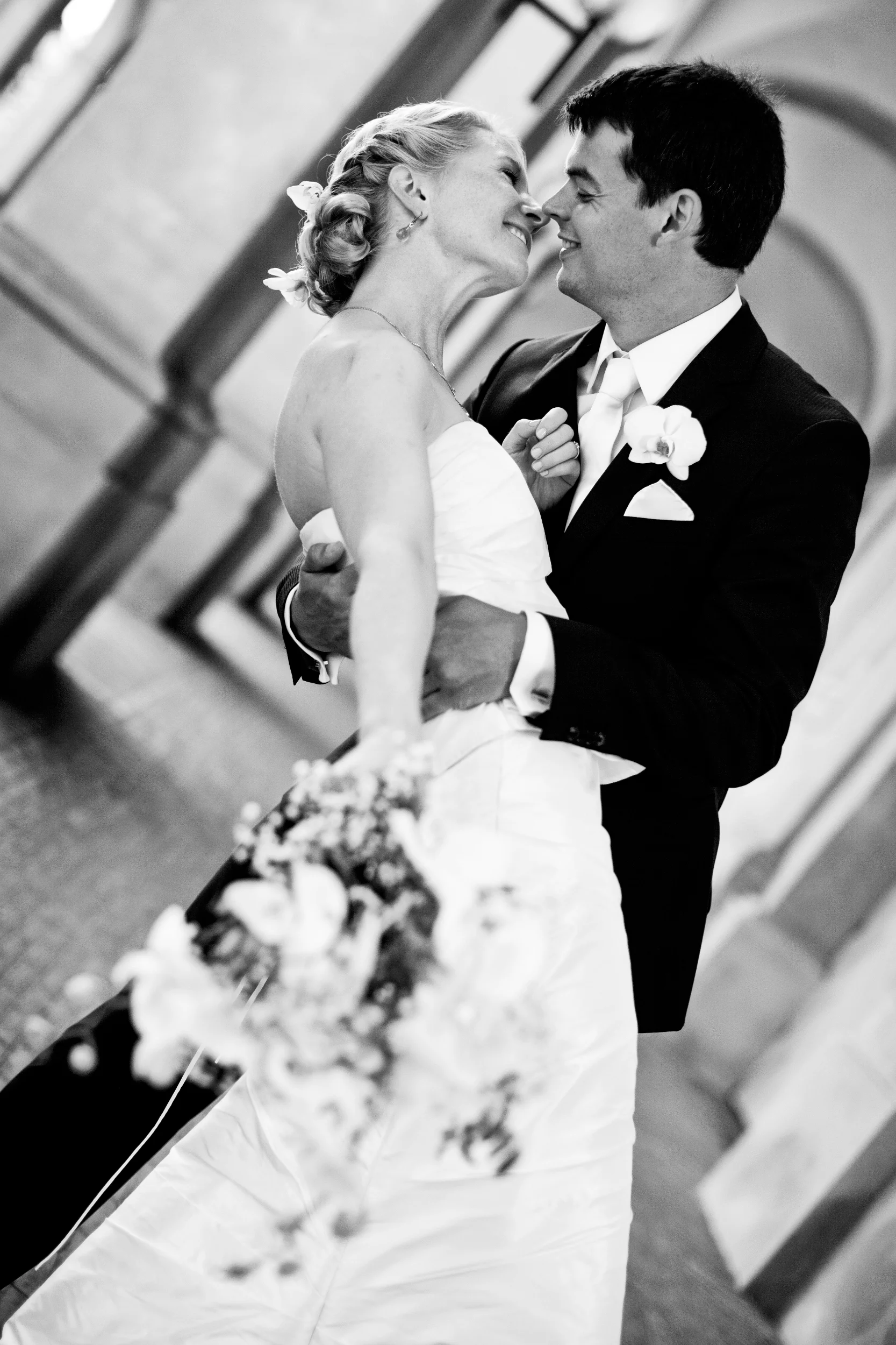 Bryllupsfotografering i sort-hvidt af brudepar med tætte blikke og smil, med bruden der holder en buket.