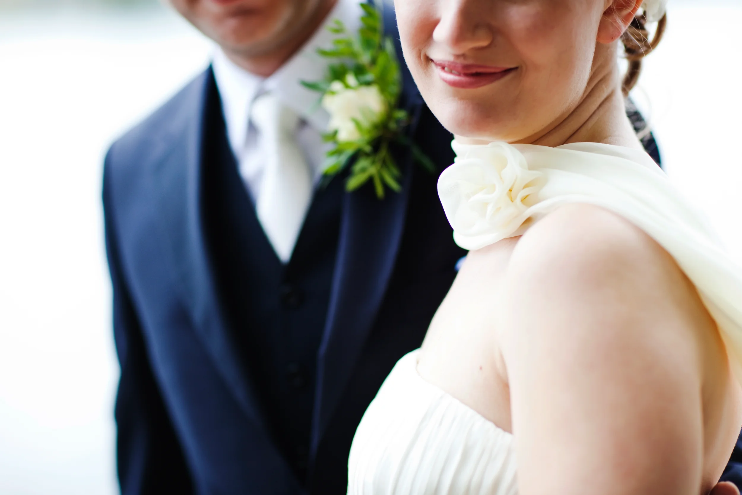 Bryllupsfotografi: Brudepar med fokus på bruden der smiler i hvid kjole og brudgom i mørkt jakkesæt med bryst