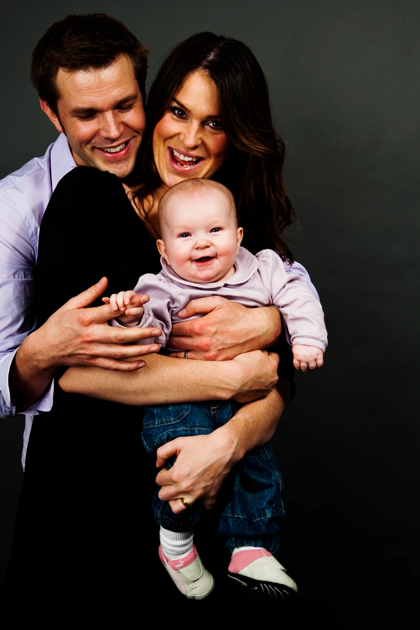 Familieportræt af glade forældre der holder deres grinende baby i et spontant og varmt øjeblik, fotograferet i Virum.