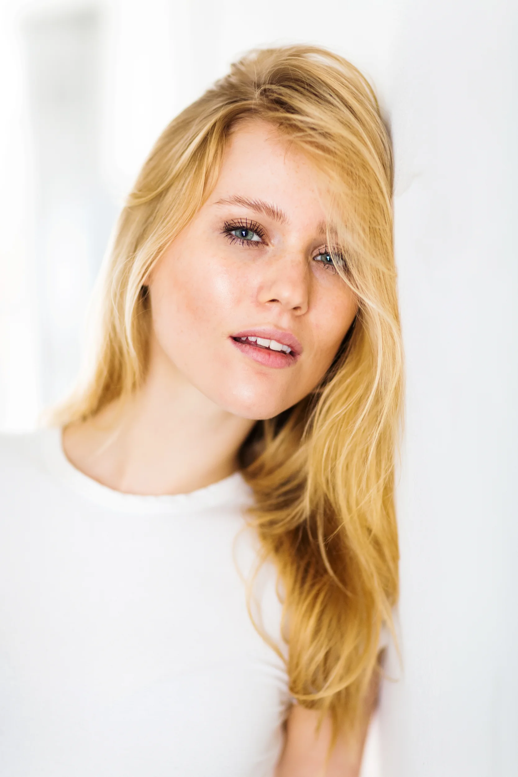 Nærbillede af ung kvinde med langt, blondt hår og blå øjne, fotograferet i blødt naturligt lys. Stemningsfuldt portrætfoto.