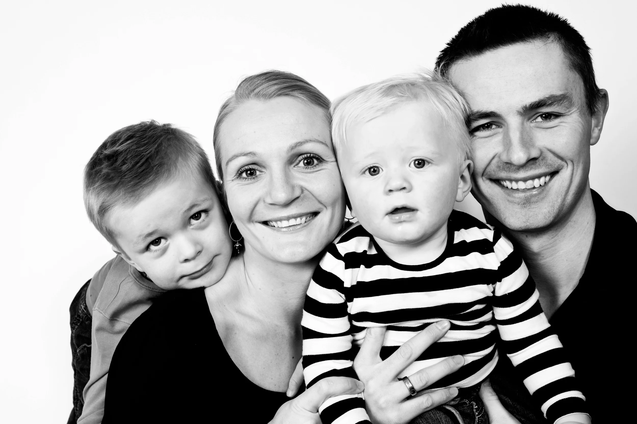Sort/hvidt familiefoto med fire smilende personer; mor, far og to små begejstrede børn i Virum.