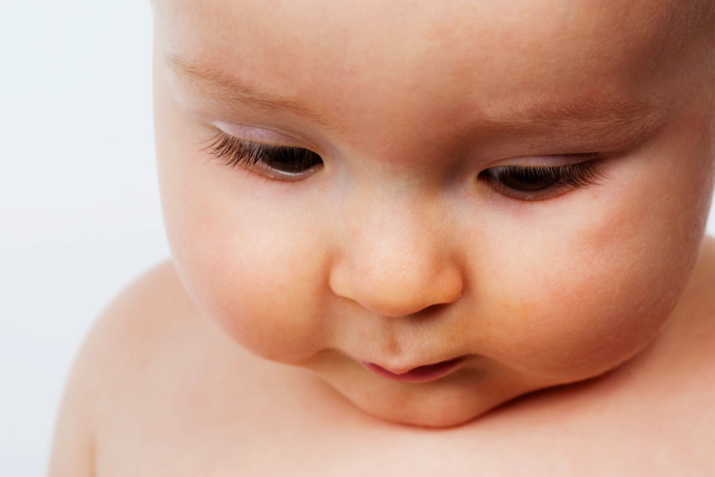 Nærportræt af baby med tænksomt udtryk, set skråt fra oven med blødt, diffust lys. Et roligt babyfotografi.