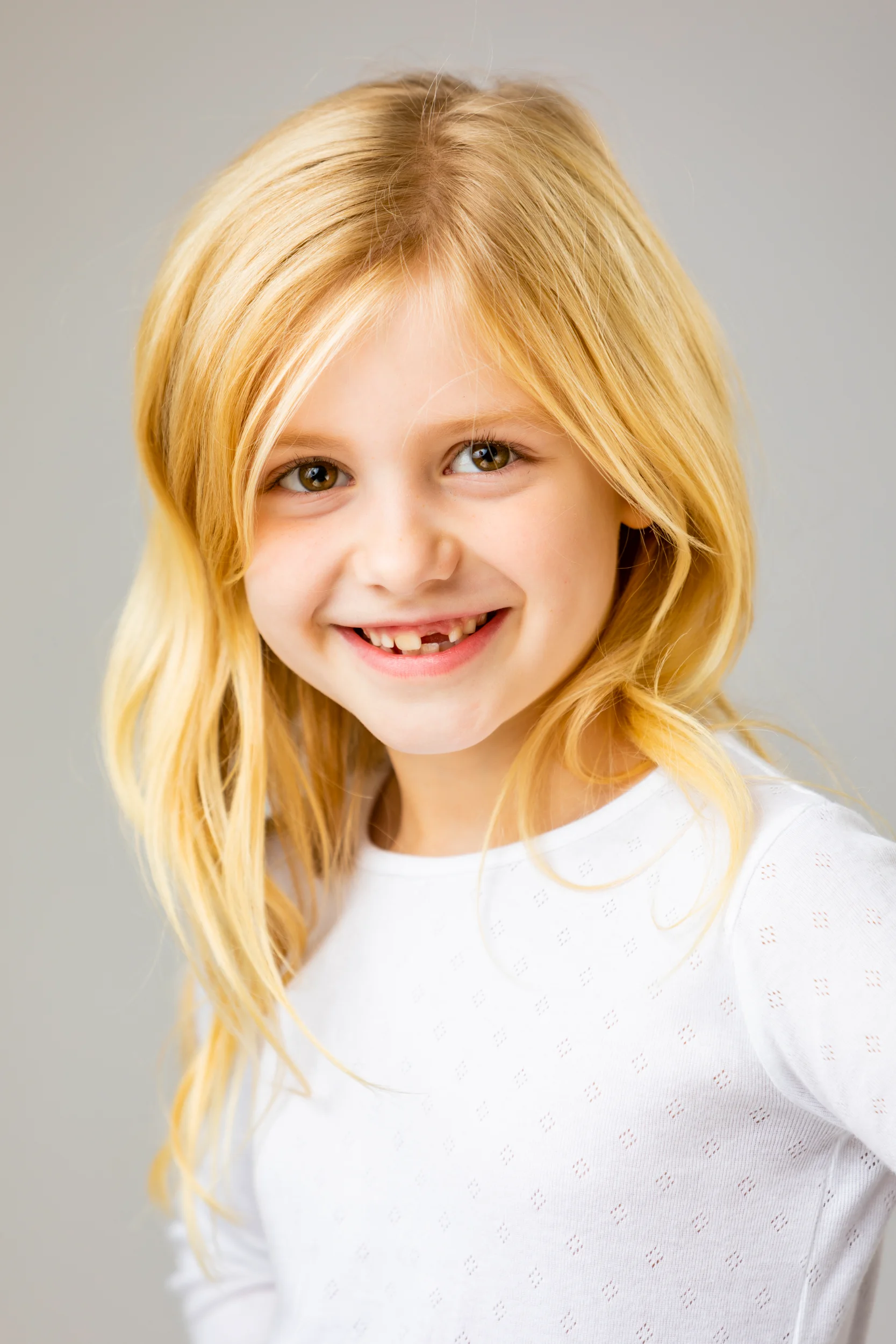 Glad blond pige med smil og manglende fortand, et charmerende børnefoto i Virum.