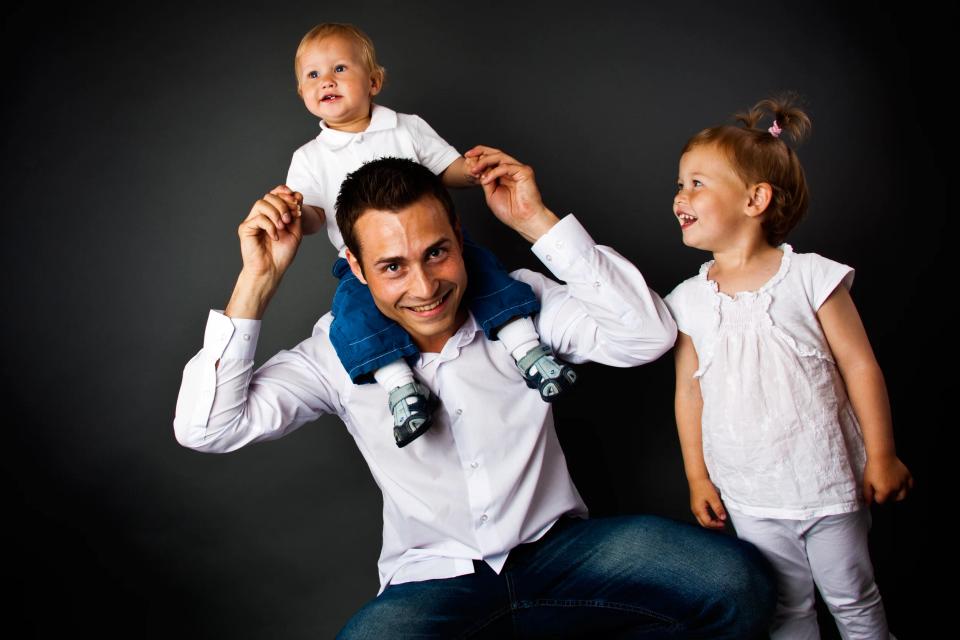 Familiefoto i studie af far med en glædestrålende dreng på skuldrene og pige ved siden af.
