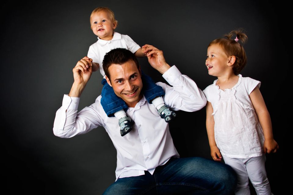Familiefoto i studie af far med en glædestrålende dreng på skuldrene og pige ved siden af.