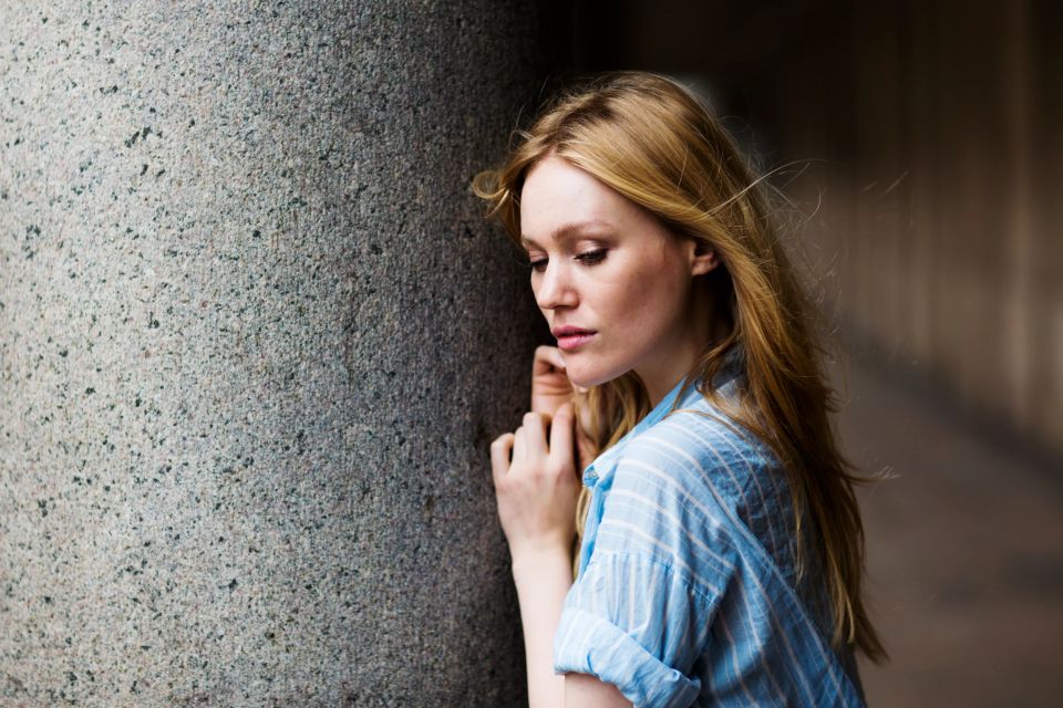 Portrætfoto af kvinde med lyst hår, der læner sig ind mod en ru mur med et eftertænksomt udtryk.