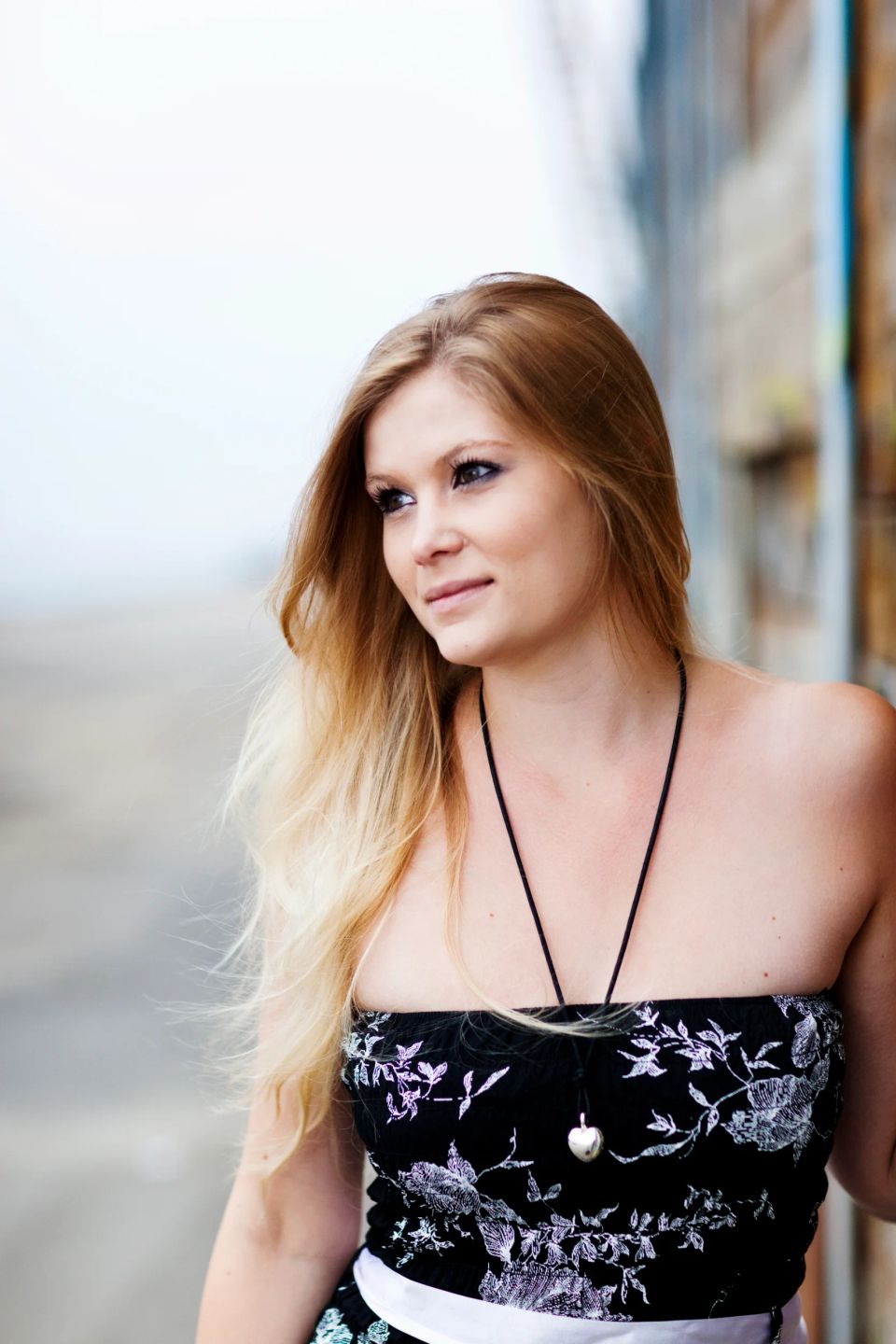 Portrætfoto af ung kvinde med langt, lyst hår og sort stropløs kjole, der ser tænksomt ud i det fjerne.