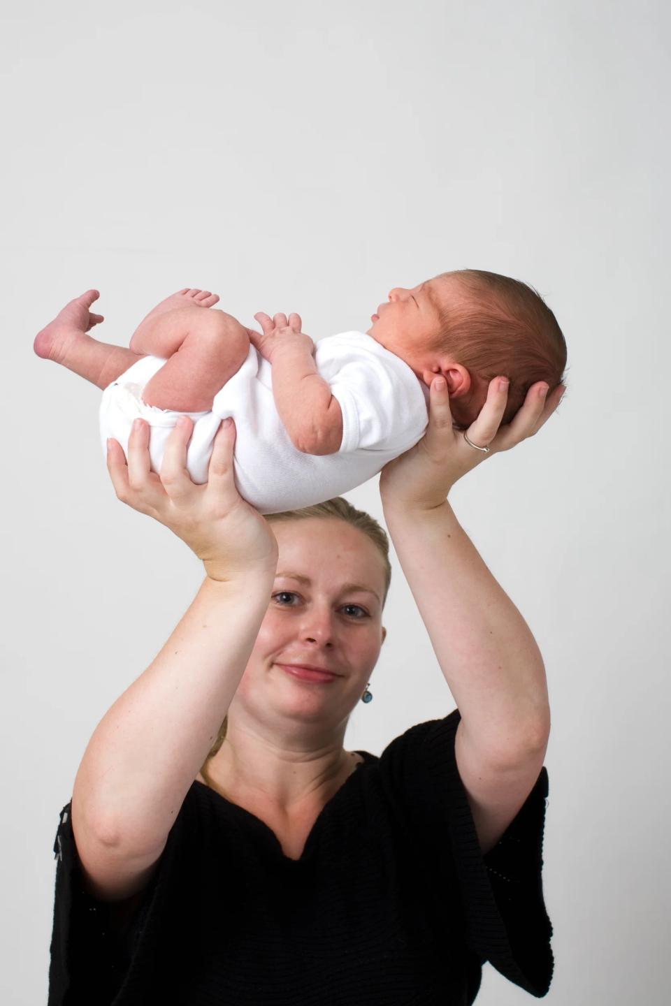 Sort-hvidt foto af en kvinde, der holder en spædbarn baby over sit hoved, med babyen liggende på ryggen.