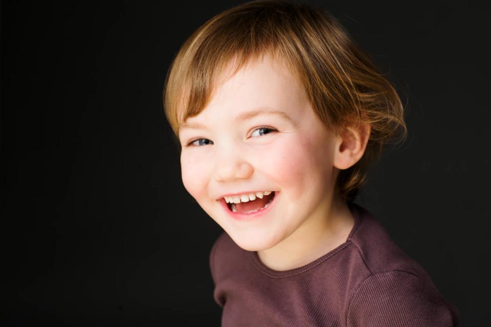 Nærbillede af en lyshåret glad pige, der griner og kigger mod venstre, fotograferet i studie mod mørk baggrund. Et børn foto.