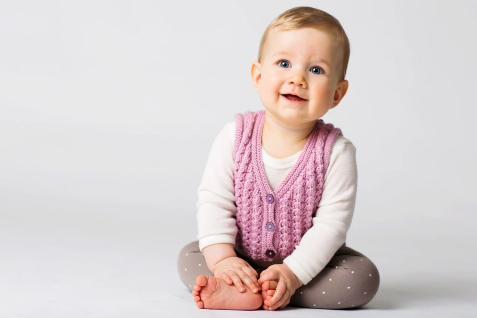 Glad baby med strålende blå øjne i pink vest til Virum babyfotografering, siddende med fokus og et smil.