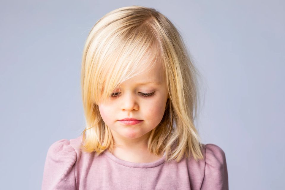 Nærbillede af et barn med blondt hår, der kigger ned. Billedet er et autentisk børneportræt med naturligt lys.