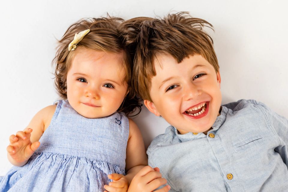 To glade børn, en pige og en dreng, ligger side om side og griner mod kameraet i et autentisk børnebillede.