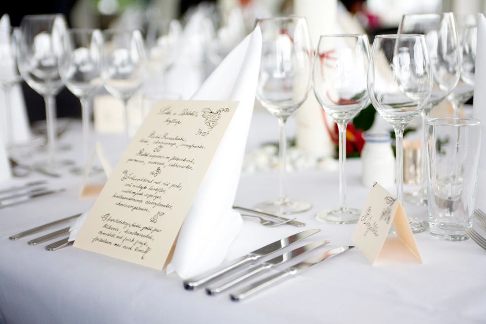 Nærbillede af elegant bryllupsbord med hvid dug, menukort, hvid stofserviet, bestik og vinglas i smukt lys.