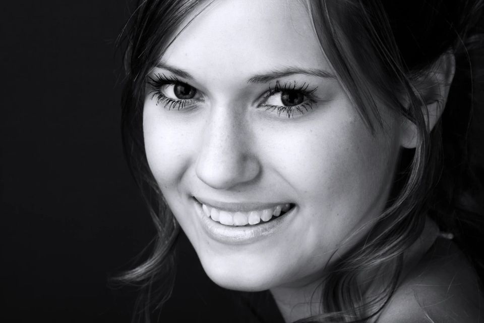 Portrætfoto af smilende kvinde med lysebrunt hår, fremhævet af blødt, naturligt lys og en varm glød.