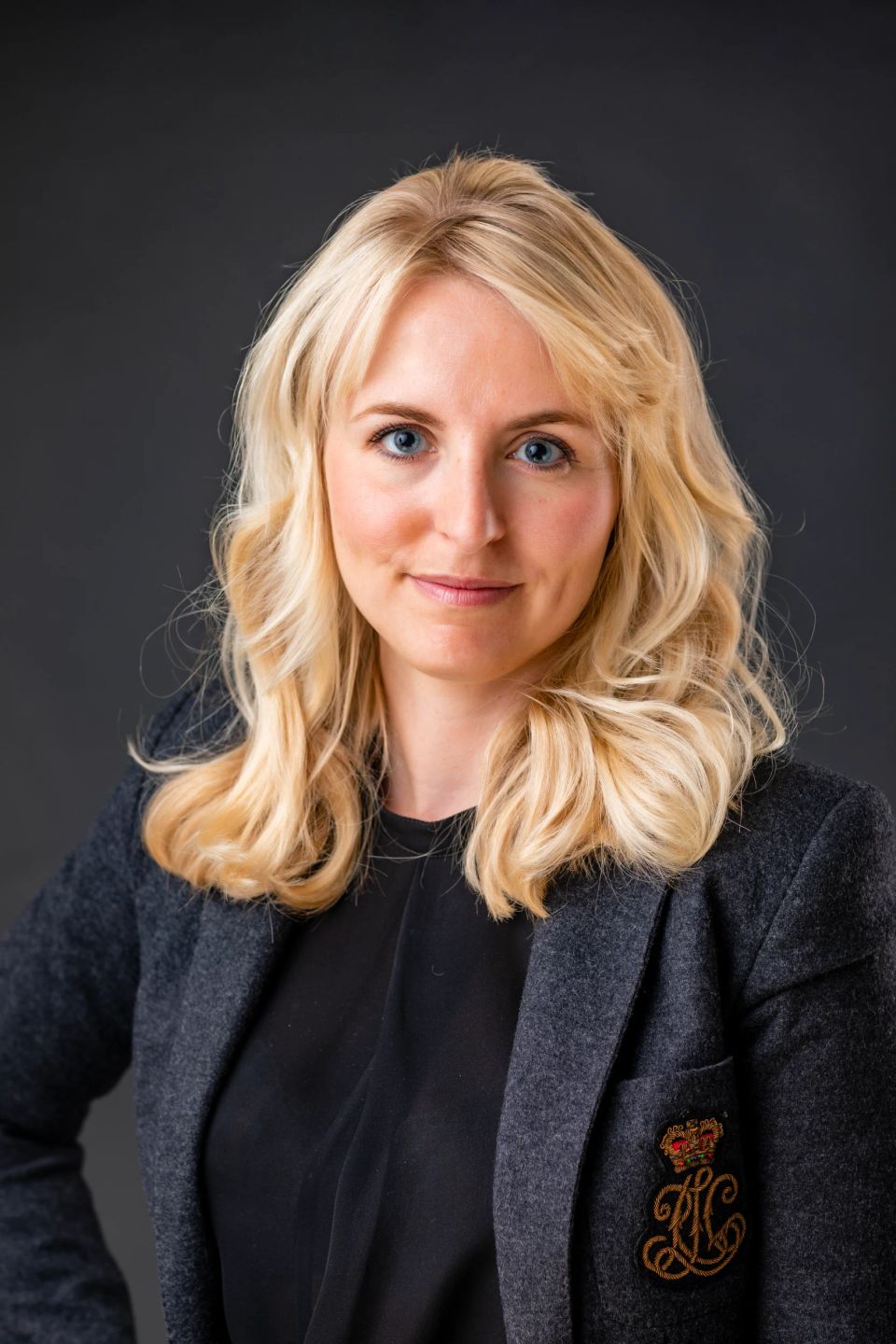 Nærbillede af kvinde med blondt hår og intense blå øjne, klædt i mørk blazer, et ægte portrætfoto.