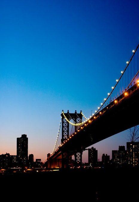 New Yorks Manhattan Bridge oplyst i mørket, med byens skyline som mørk silhuet mod aftenhimlen. Et andet fotomotiv.