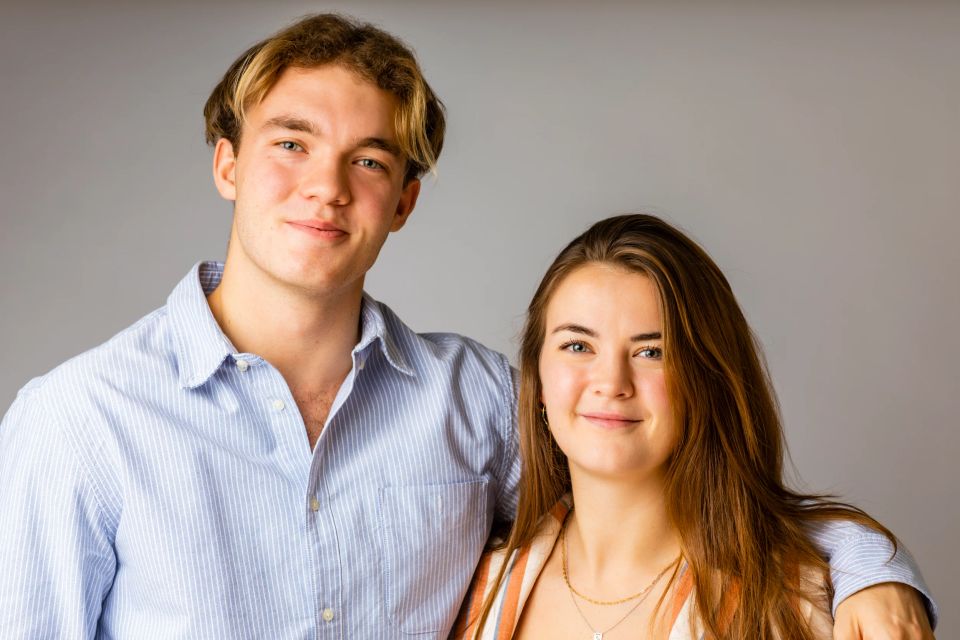 Familieportræt af to unge søskende, en dreng og en pige, der smiler varmt mod kameraet i et studie.