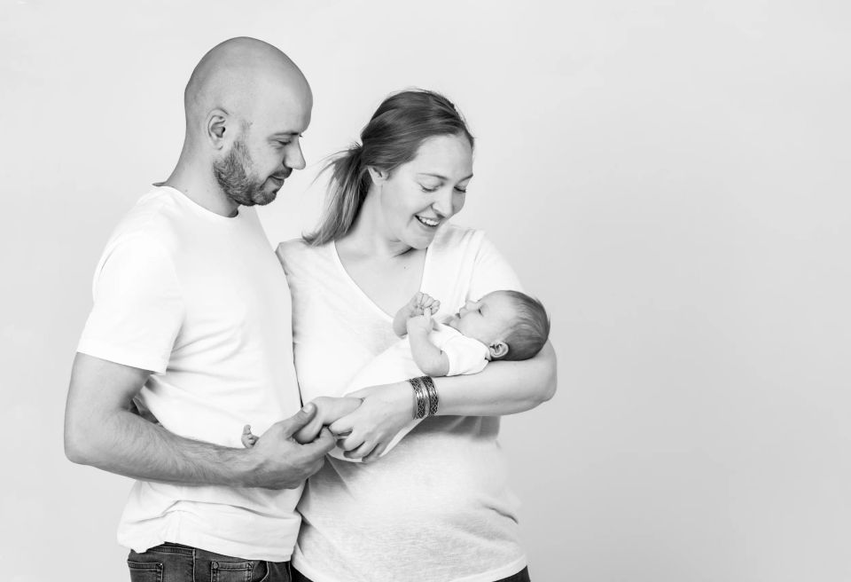 Sort-hvidt babyfotografi af nyfødt i mors arme, mens far holder den lilles fod. Hjertevarm stemning.