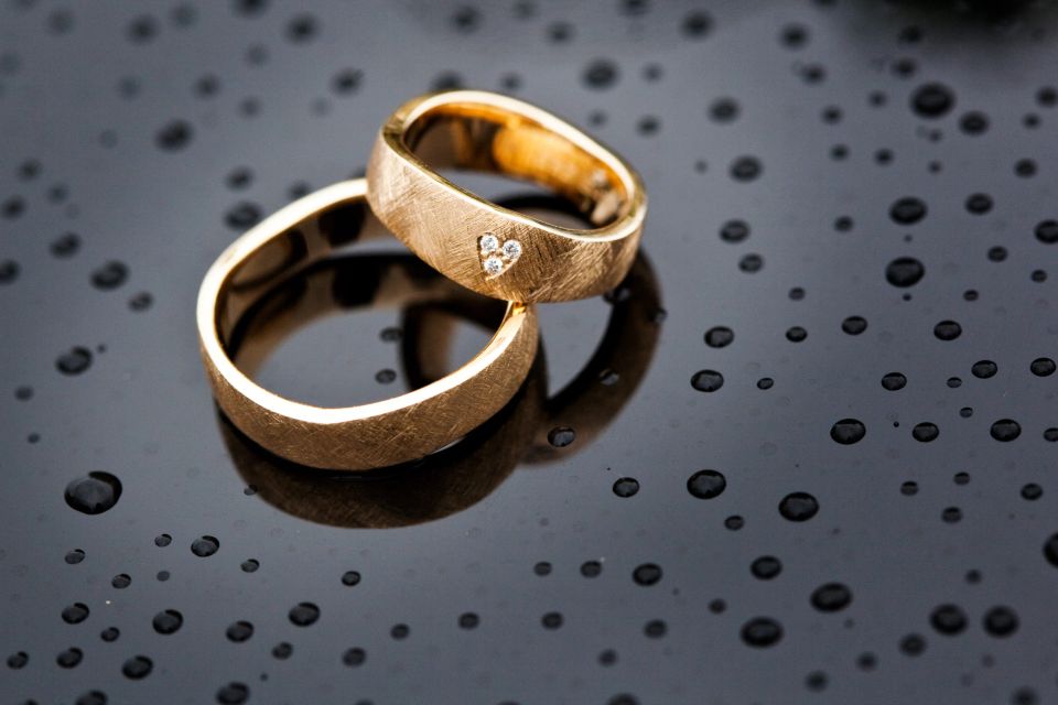 Bryllupsfotografi af et nygift par, der omfavner ved havet med en pyntet veteranbil i baggrunden. Stemningsfuldt billede.