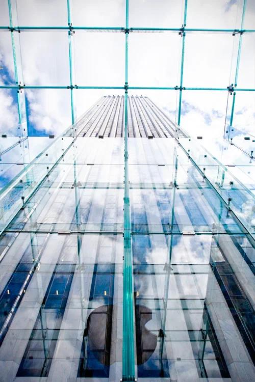 Abstrakt foto af Apple Store i New York. Bygningens glasfacade reflekterer himmel, skyer og byens anden arkitektur.