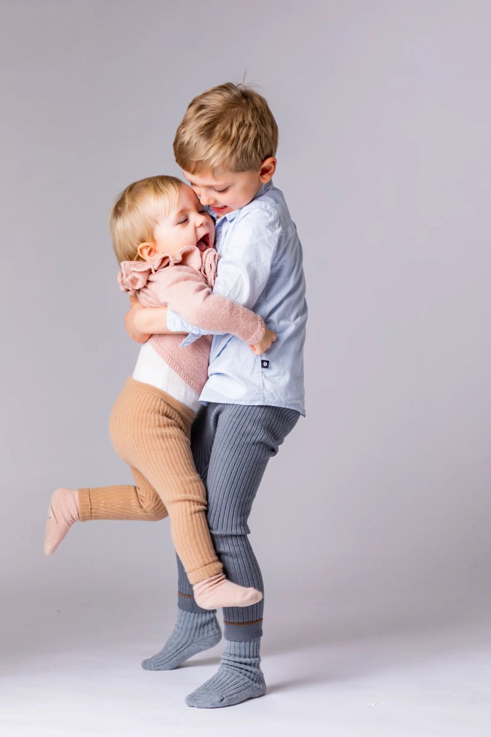 Børn: En glad dreng giver sin lillesøster et varmt kram. Hun griner med åben mund, mens han holder og løfter hende blidt.