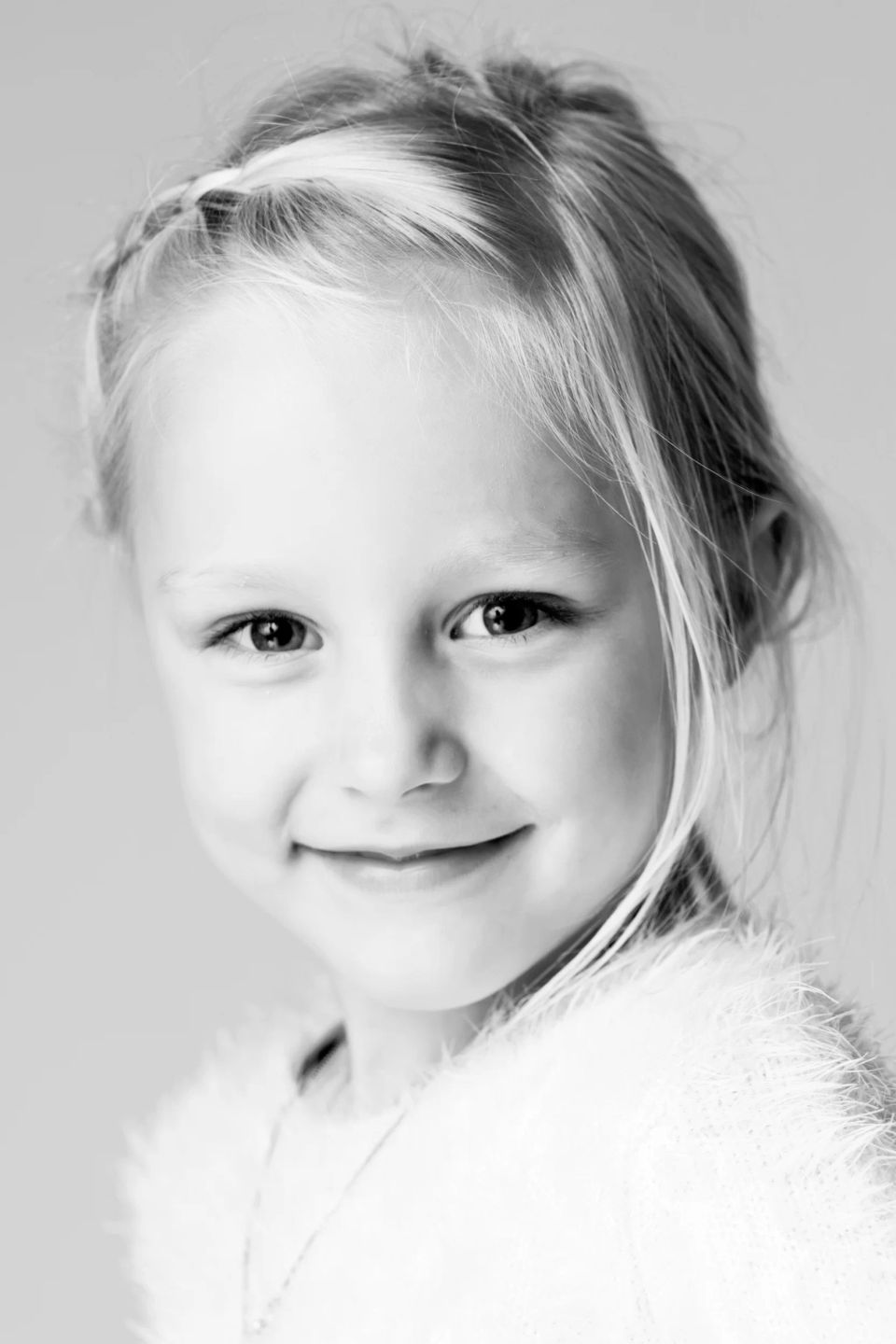 Sort-hvidt børnefoto af smilende, glad lille pige med lyst hår og fletning i Virum, blødt lys.